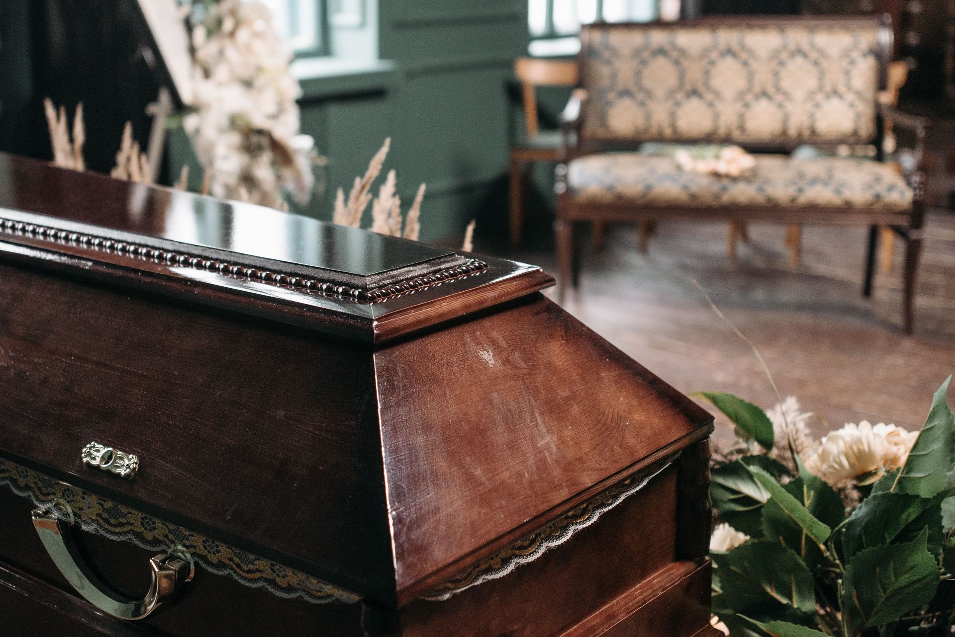 Elegant wooden coffin surrounded by floral arrangements in an indoor funeral setting, capturing a somber mood.